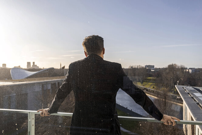 Ein Mann von hinten, Carsten Schneider, blickt von einem Balkon des Kanzleramt auf den Tiergarten