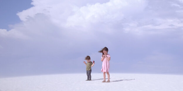 Ein Mädchen und ein Junge stehen in einer surrealen Landschaft vor großen Wolken