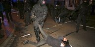 Ein Polizist zieht das Bein eines am Boden liegenden Aktivisten nach oben.