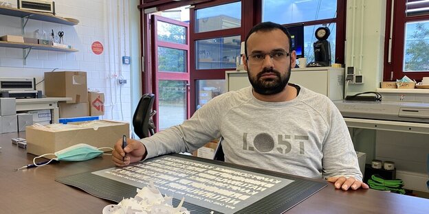 Raheel Afzal in der Buchbinderei der Stephanus-Stiftung ​in Berlin-Oberschöneweide, er sitzt an einem Schreibtisch