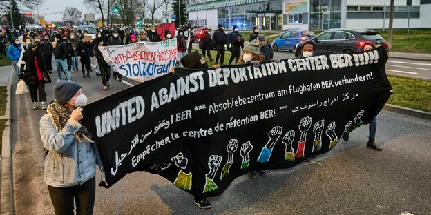 Eine Gruppe von Menschen Demonstriert mit Bannern, wie der im Vordergurnd wo United against deportation center BER draufsteht