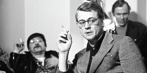 Alexander Kluge raucht, hinter ihm sitzt Rainer Werner Faßbinder