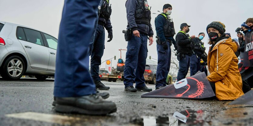 Das Foto zeigt Polizisten, die vor sitzenden Menschen stehen, die eine Autobahnauffahrt blockieren.