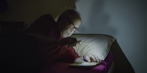 Der Regisseur Godard im Bett, bei wenig Licht lesend