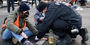 Ein Polizist versucht die Hand einer Aktivistin vom Boden zu lösen. Sie hatte sich an die Strasse geklebt