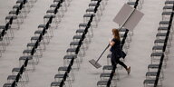 Eine Frau trägt ein Schild durch leere Stuhlreihen