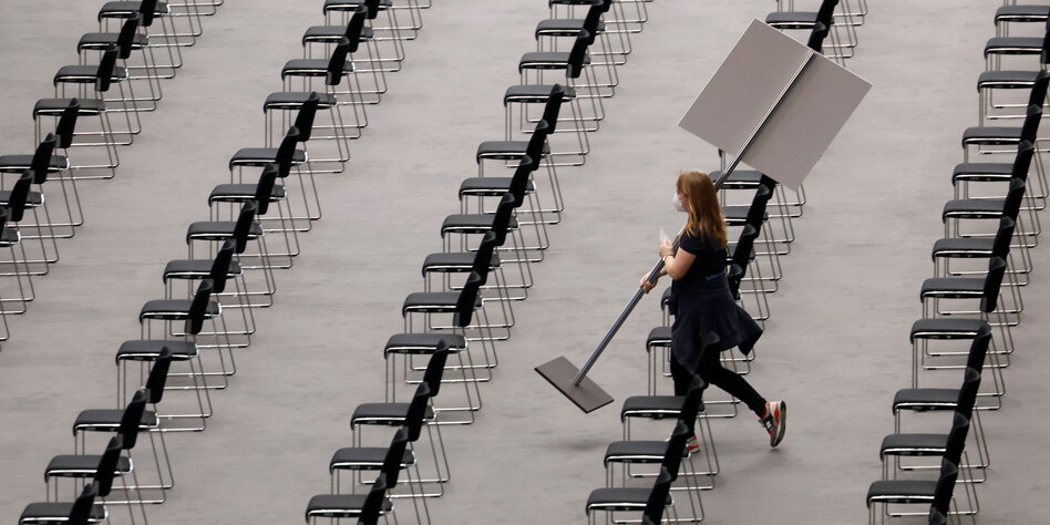 Eine Frau trägt ein Schild durch leere Stuhlreihen