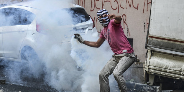 Ein Mann mit einer Maske steht in Rauchschwaden von Tränengas
