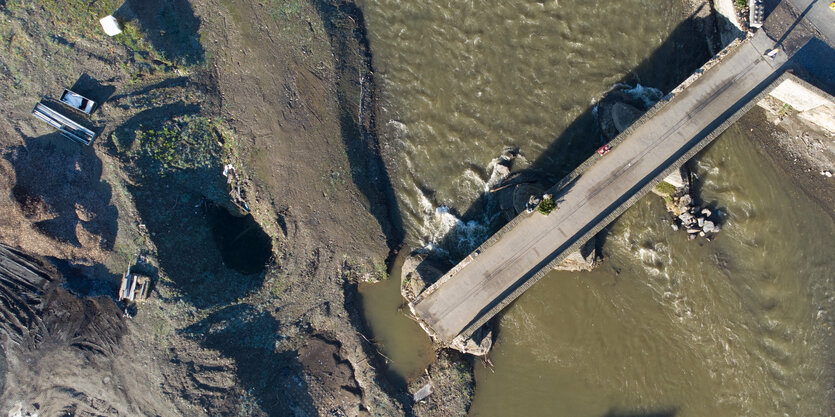 Blick von oben auf zerstörte Bodenbrücke mit Schlamm und Wasser drumherum