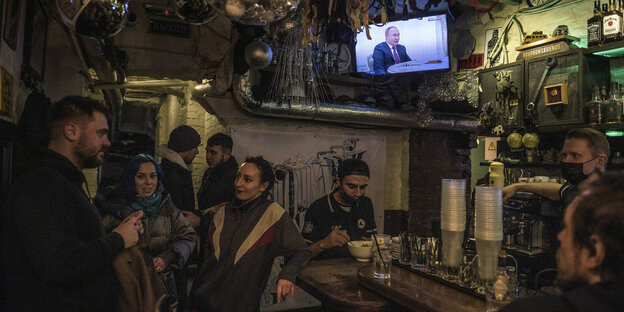 Menschen in einer Bar in Moskau, im Hintergrund eine Fernseher, auf dem Putin zu sehen ist.
