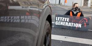 Ein Mann mit Warnweste sitzt auf einer Autobahnausfahrt und hält ein Schild mit der Aufschrift "Letzte Generation"