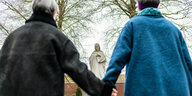 Zwei Personen stehen Hand in Hand vor einer Statue von Maria.