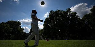 Ein Mann auf einer Wiese wirft einen Ball in die Luft.