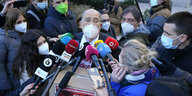 Ein älterer Mann umringt von Journalisten mit Mikrofonen