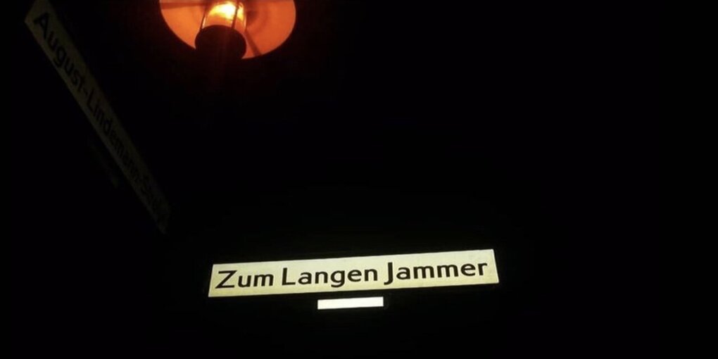 Man sieht ein Straßenschild, auf dem steht Zum langen Jammer. Es wird von einer Straßenlaterne beleuchtet