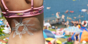 Rückenansicht eines Mädchens im Bikini mit einer aus Sonnenmilch gemalten Sonne