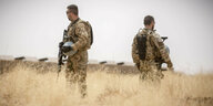 Zwei Soldaten der Bundeswehr stehen Rücken an Rücken mit Waffen in der Hand auf einem ausgetrockneten Feld