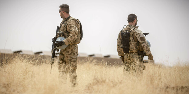 Zwei Soldaten der Bundeswehr stehen Rücken an Rücken mit Waffen in der Hand auf einem ausgetrockneten Feld
