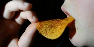 Eine Detailaufnahme eines Kindes das Chips in den Mund schiebt