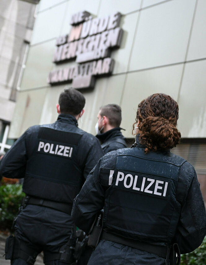 PolizistInnen von hinten vor einem Gebäude, in der Unschärfe steht "Die würde des Menschen ist unantastbar"