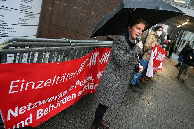 Eine Frau steht vor einem roten Spruchband "Einzeltäte" und viele Strichlisten"