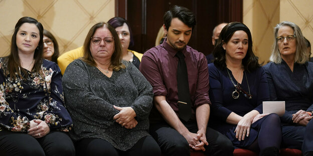 Eine Gruppe von Menschen sitzt mit traurigem Gesicht in einem Saal