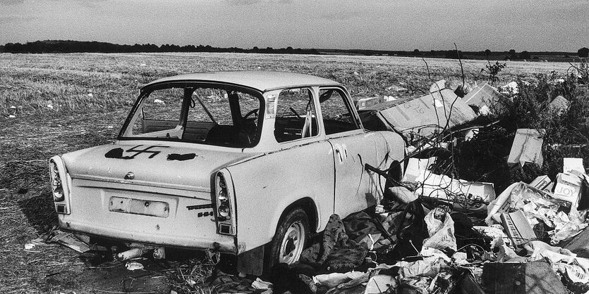 Ein alter Trabbi steht in der Landschaft, auf die Kofferraumhaube ist ein Hakenkreuz gemalt