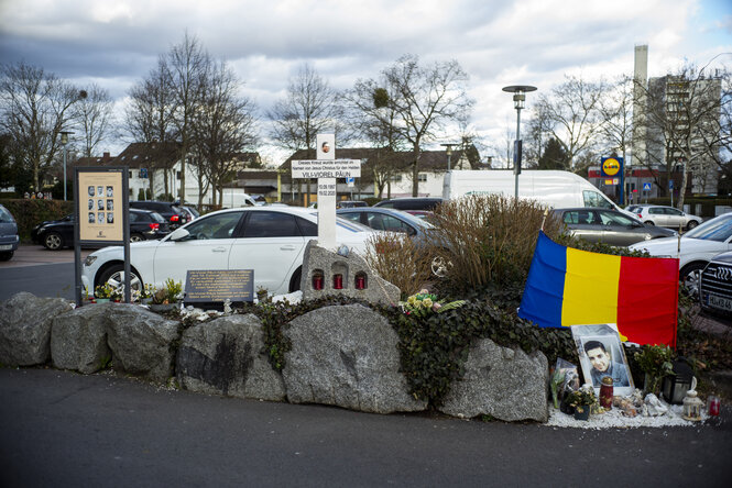 Neben einem Parkplatz ein Kreuz und Gedenkort mit rumänischer Flagge