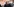 Eine blonde Frau im dunklen Mantel, dahinter ein Mann mit FFP2-Maske