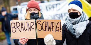 Zwei Demonstrantinnen halten Schilder in die Kamera mit der Aufschrift Braun? Schweig!