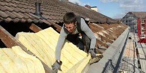 Eine Dachdeckerin bringt Mineralwolle zur Wärmedämmung auf dem Dach eines Hauses an