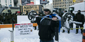 Ein Mann hebt eine Hantel auf schneebedeckter Straße. Im Hintergrund stehen Polizisten, überall hängen Protestplakate