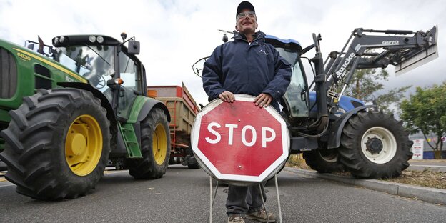 Ein Bauer vor zwei Traktoren, die quer auf der Straße stehen.