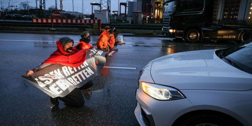 Personen mit Plakaten blockieren eine Straße.