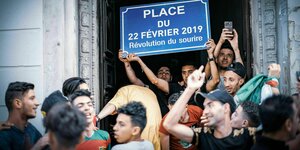 Junge Männer hlaten ein Schild hoch: Platz des 22.Februars 2019 Revolution des Lächelns