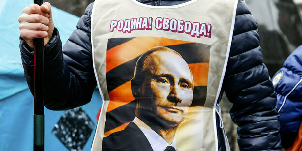 ein Demonstrant trägt eine Weste mit dem Portrait Putins auf dem steht: Mutterland, Freiheit
