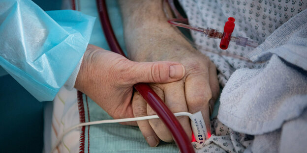 Eine Krankenschwester versorgt einen schwer an Corona erkrankten Patienten auf der Intensivstation des Klinikums in Fulda und hält dabei die Hand des Mannes.