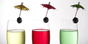 In je einem Sektglas drei farbige Cocktails mit Schirmchen und Olive dekoriert