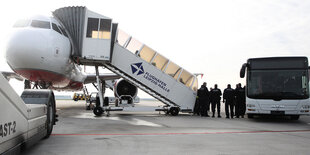 Polizisten stehen zwischen einem Flugzeug und einem Bus