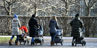 unge Muetter schieben ihre Kinderwaegen durch den Park