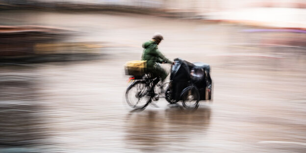 Ein Mann fährt an einem regnerischen und windigen Tag mit dem Lastenfahrrad