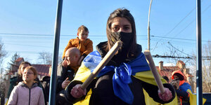 Eine junge Frau trommelt mit ukrainischer Flagge um die Schultern