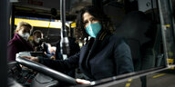 Bettina Jarasch mit grüner Maske an einem Bus-Lenkrad