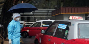 Ein Mann in Schutzkleidung schaut auf ein rotes Taxi