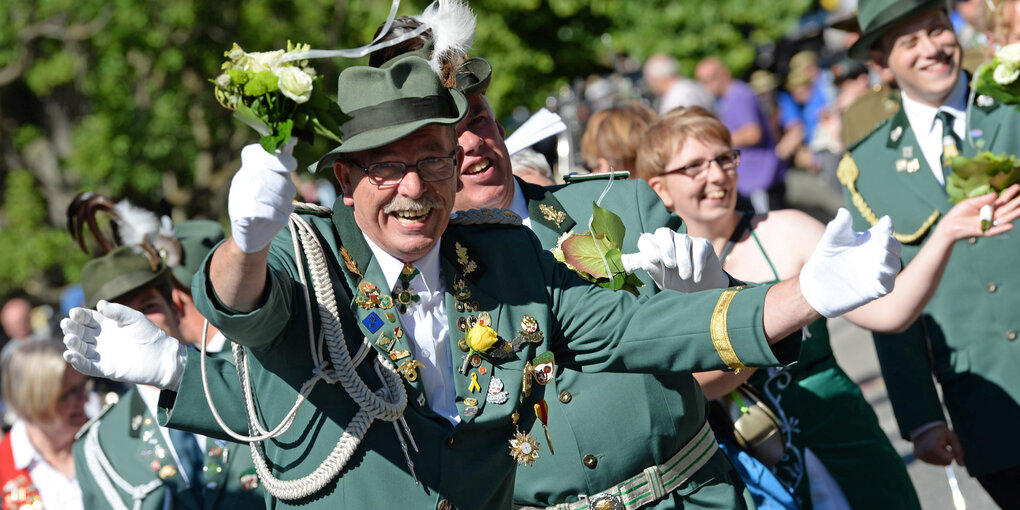 Ein Mann in Schützenuniform winkt enthusiastisch mit einem Blumenstrauß in der Hand in die Kamera, um ihn herum weitere Teilnehmer des Festumzuges 2018