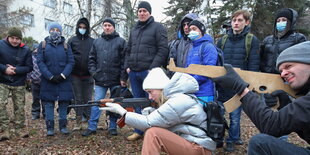 Eine Frau mit Gewehr, ein Mann mit Pappgewehr, Schaulustige im Hintergrund