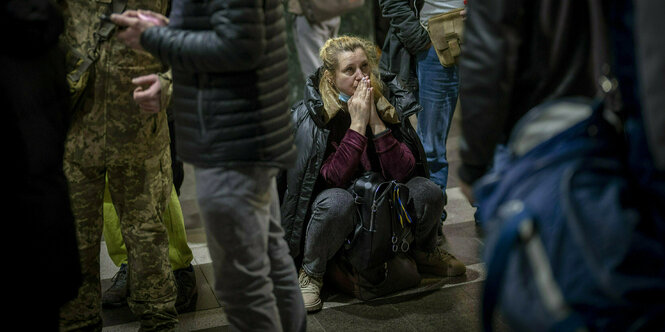 Eine junge Frau hockt auf dem Boden, umgeben von Menschen ,die stehen