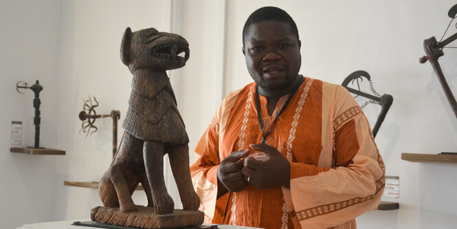 Ein Afrikaner im orangenfarbenen Gewand im Museum vor einer Skulptur