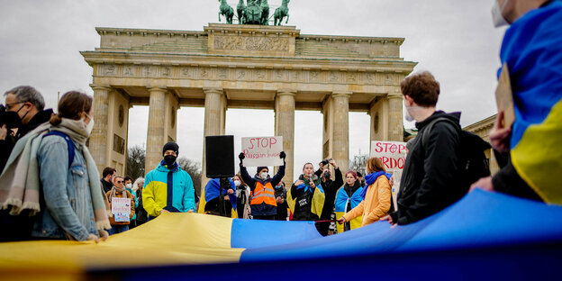 Demonstrant:innen vor dem Brandenburger Tor mit gelb-blauen Fahnen