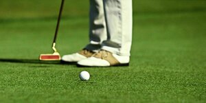 Detailansicht: Schuhe eines Golfers, der Schläger und ein Ball auf grünem Rasen